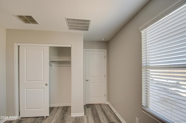 unfurnished bedroom featuring a closet, wood finished floors, visible vents, and baseboards