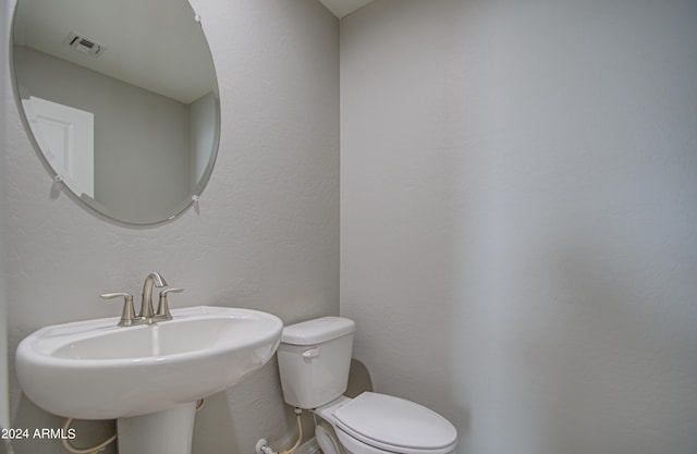 half bathroom featuring toilet, visible vents, a sink, and a textured wall