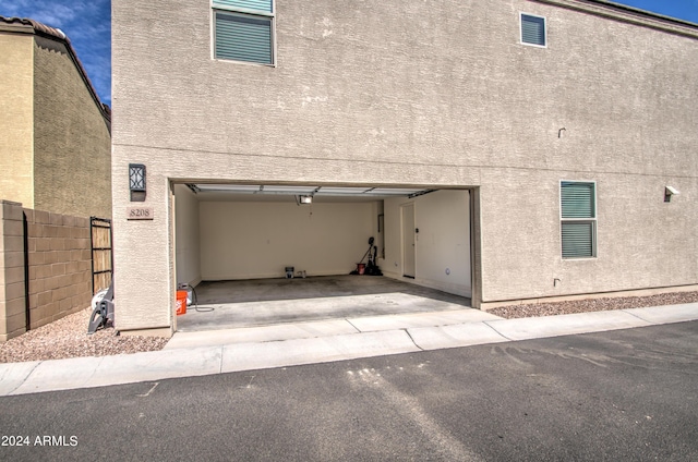 garage featuring driveway, fence, and a garage door opener