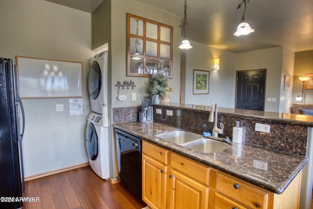 kitchen with sink, dark hardwood / wood-style flooring, dark stone countertops, black appliances, and stacked washer and clothes dryer