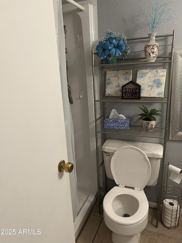 bathroom featuring a stall shower, tile patterned flooring, a textured wall, and toilet