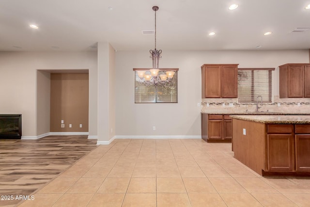 kitchen with pendant lighting, sink, backsplash, light stone counters, and a chandelier