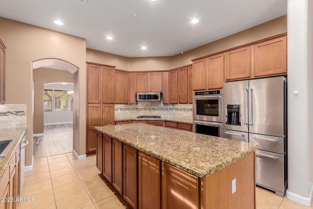 kitchen featuring stainless steel appliances, a center island, light stone countertops, and light tile patterned flooring