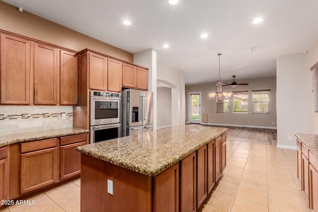 kitchen with pendant lighting, appliances with stainless steel finishes, a kitchen island, decorative backsplash, and light stone counters