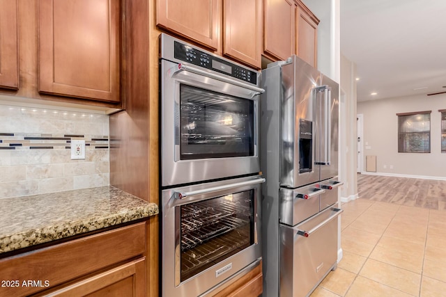 kitchen with light stone countertops, backsplash, light tile patterned floors, and appliances with stainless steel finishes