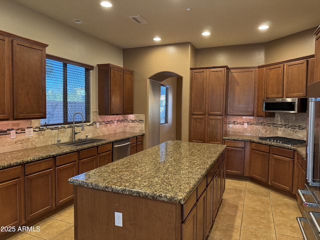 kitchen featuring appliances with stainless steel finishes, sink, dark stone counters, light tile patterned flooring, and a kitchen island