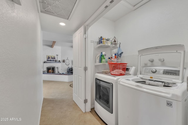 laundry area with laundry area, light tile patterned floors, a large fireplace, visible vents, and washer and dryer