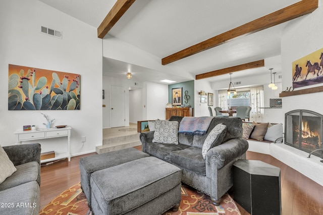 living area featuring a lit fireplace, beam ceiling, visible vents, and wood finished floors