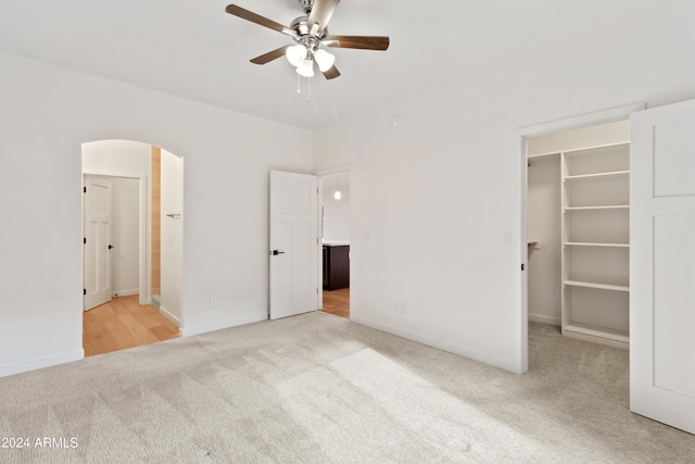 unfurnished bedroom featuring a walk in closet, light colored carpet, a closet, and ceiling fan