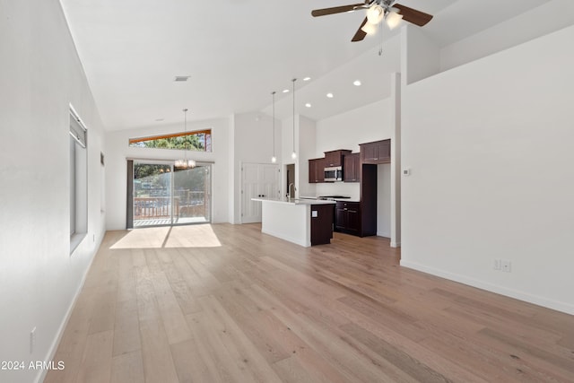 unfurnished living room with light hardwood / wood-style flooring, high vaulted ceiling, ceiling fan with notable chandelier, and sink