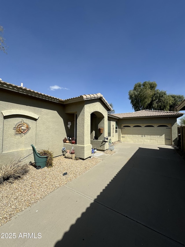 exterior space featuring driveway, a tiled roof, an attached garage, and stucco siding