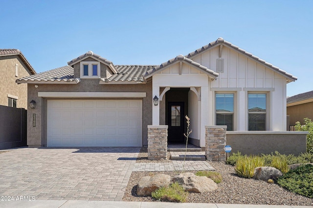 view of front of home featuring board and batten siding, a tile roof, stucco siding, decorative driveway, and a garage