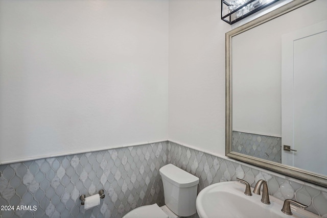 half bath featuring toilet, a wainscoted wall, and a sink