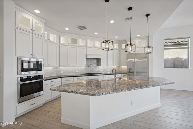 kitchen featuring wood finish floors, visible vents, built in appliances, and decorative backsplash