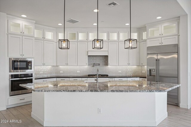 kitchen with built in appliances, a center island with sink, and hanging light fixtures