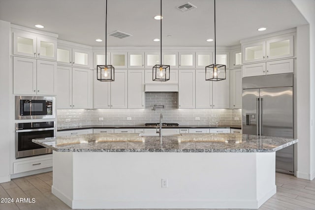 kitchen with visible vents, built in appliances, a kitchen island with sink, and light wood finished floors