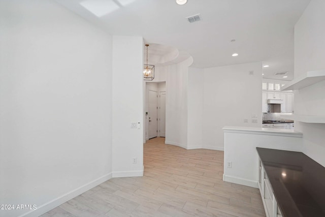 kitchen with visible vents, light wood-style flooring, tasteful backsplash, white cabinets, and baseboards