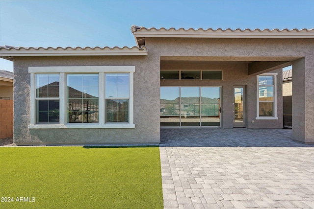 view of exterior entry with a patio area, a lawn, and stucco siding