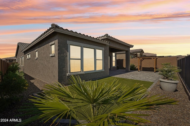 back of property at dusk with a patio area, stucco siding, a tiled roof, and a fenced backyard