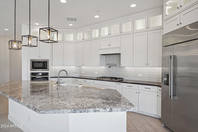 kitchen with white cabinets, visible vents, built in appliances, and a sink