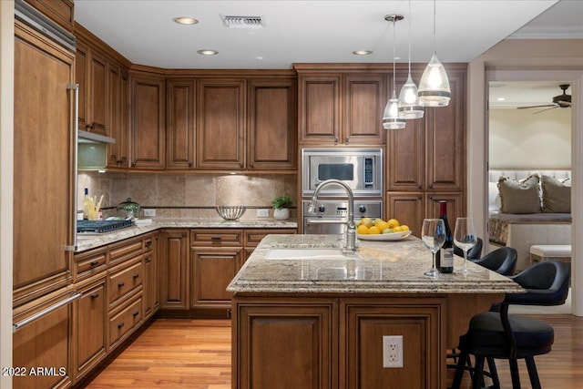 kitchen with light stone countertops, appliances with stainless steel finishes, light wood-type flooring, a breakfast bar, and a center island with sink