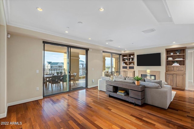 living room with built in features, wood-type flooring, and ornamental molding