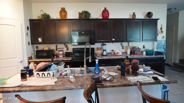 1309 W Park St, Phoenix, AZ 85041 - kitchen with black appliances, tile patterned flooring, a breakfast bar area, dark brown cabinetry, and dark countertops