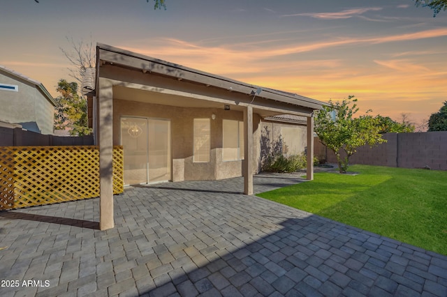 back house at dusk with a lawn and a patio area