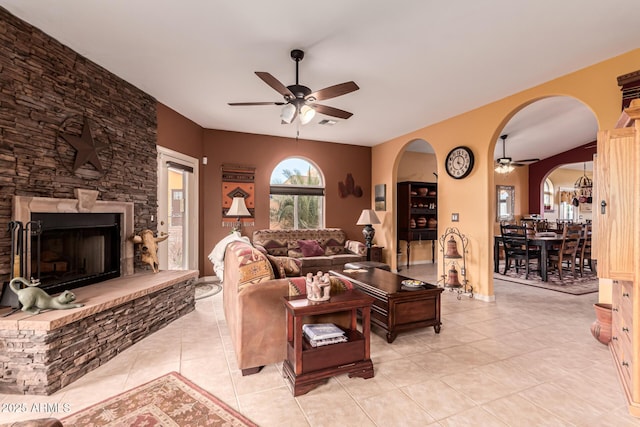 living room with arched walkways, a stone fireplace, a ceiling fan, and light tile patterned flooring