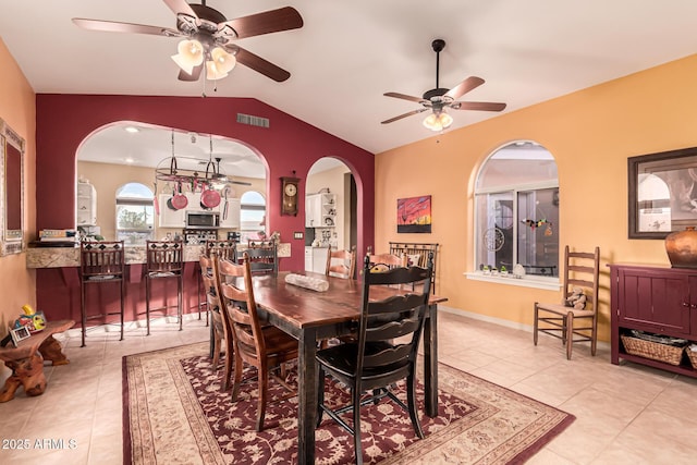 dining room featuring visible vents, lofted ceiling, light tile patterned flooring, arched walkways, and a ceiling fan