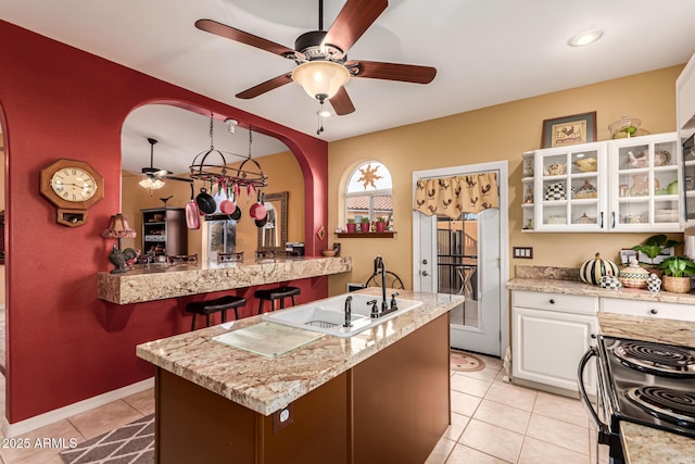kitchen with ceiling fan, arched walkways, white cabinetry, glass insert cabinets, and light tile patterned flooring