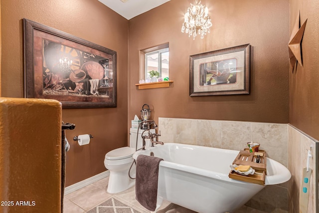 bathroom with toilet, a freestanding tub, a notable chandelier, and tile patterned floors