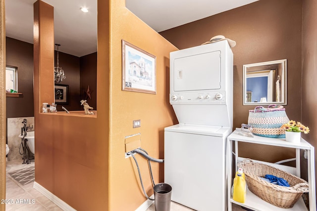laundry room with laundry area, tile patterned floors, stacked washer / dryer, and an inviting chandelier
