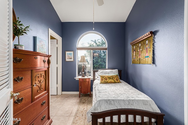 bedroom with a ceiling fan, vaulted ceiling, light tile patterned floors, baseboards, and a textured wall