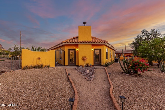 view of front of property featuring a tiled roof, a chimney, a gate, fence, and stucco siding
