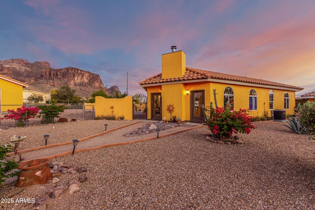 view of front of home with a tile roof, a gate, a mountain view, a chimney, and central air condition unit