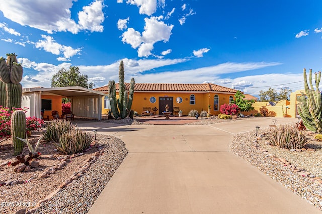 view of front of property featuring a tiled roof, an attached carport, curved driveway, and stucco siding