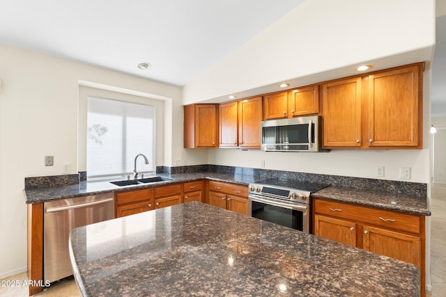 kitchen featuring vaulted ceiling, dark stone countertops, brown cabinetry, stainless steel appliances, and a sink