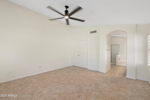 empty room with light tile patterned floors, a ceiling fan, visible vents, baseboards, and arched walkways