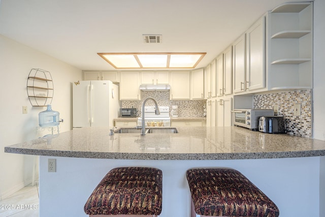 kitchen with light stone counters, visible vents, backsplash, freestanding refrigerator, and a sink