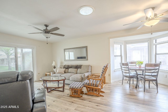 living area with light wood-style floors, a wealth of natural light, baseboards, and a ceiling fan