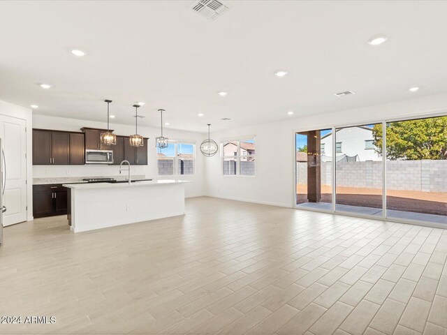 kitchen featuring dark brown cabinetry, stainless steel appliances, pendant lighting, a center island with sink, and light wood-type flooring