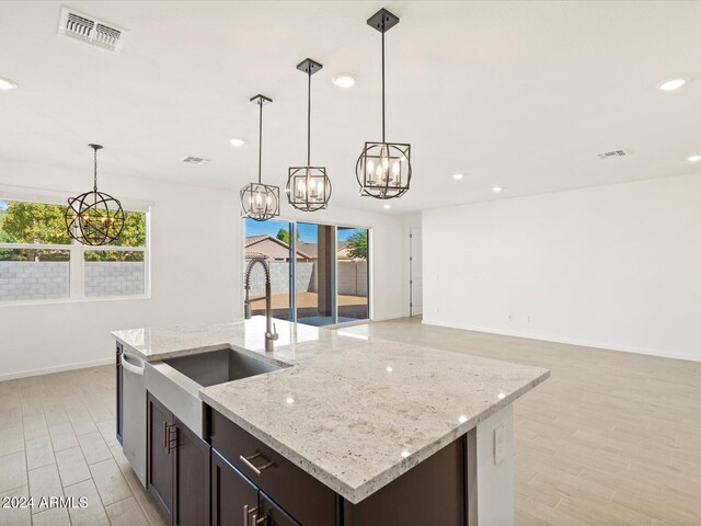 kitchen featuring light stone counters, light hardwood / wood-style flooring, pendant lighting, and dark brown cabinets