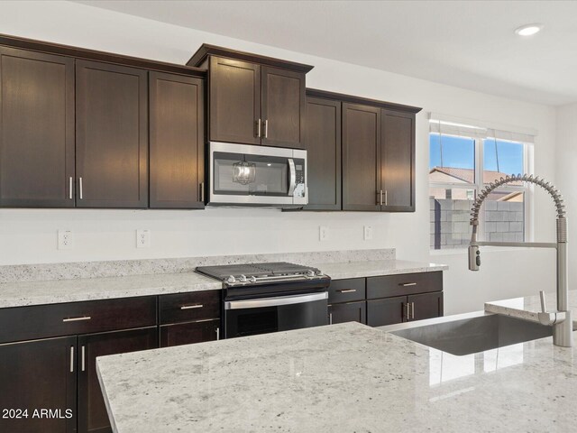 kitchen featuring light stone countertops, dark brown cabinets, stainless steel appliances, and sink