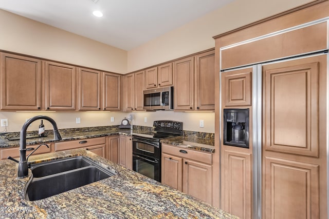 kitchen with black range with electric stovetop, dark stone countertops, sink, and paneled fridge