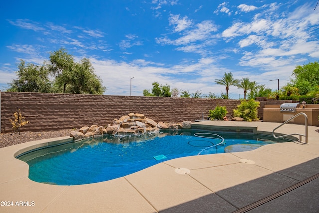 view of pool with pool water feature, a patio area, and an outdoor kitchen