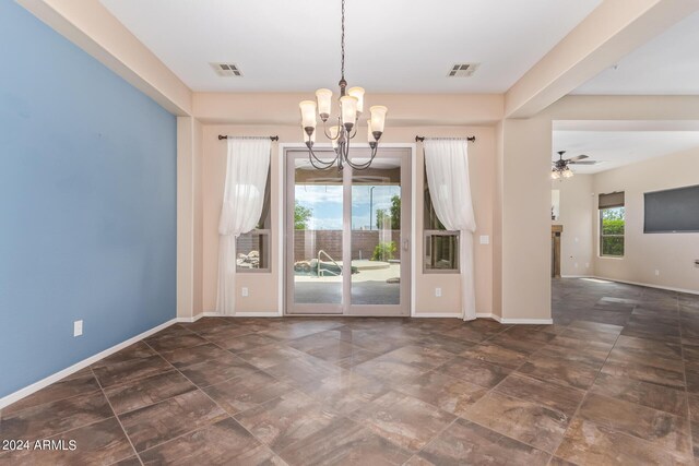 unfurnished dining area with dark tile patterned floors and ceiling fan with notable chandelier