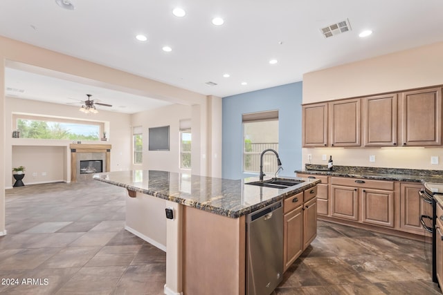 kitchen with sink, a kitchen island with sink, dark stone countertops, a tiled fireplace, and stainless steel dishwasher