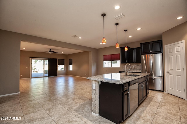 kitchen featuring sink, light stone counters, hanging light fixtures, appliances with stainless steel finishes, and an island with sink