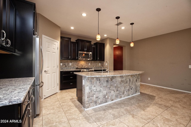 kitchen featuring appliances with stainless steel finishes, decorative light fixtures, light stone countertops, and a kitchen island with sink